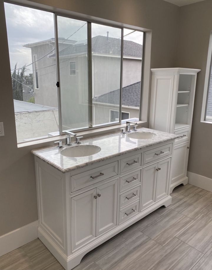 White double vanity with stone top and matching linen cabinet under a wide window